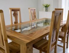 a wooden table with glass top and four chairs around it in a white room next to a window