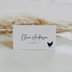 a place card sitting on top of a table next to some dried grass and a plant