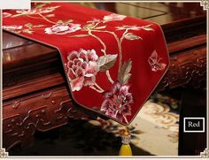 a red table runner with pink flowers on it and a yellow tassel hanging from the end