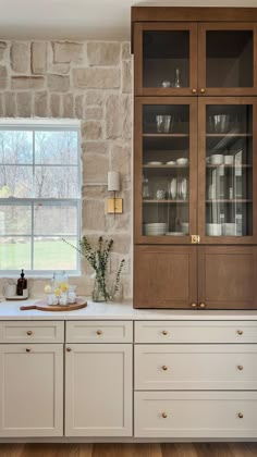 a kitchen with white cabinets and wood flooring next to a brick wall that has a window