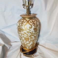 a gold and white vase sitting on top of a white cloth covered floor next to a lamp