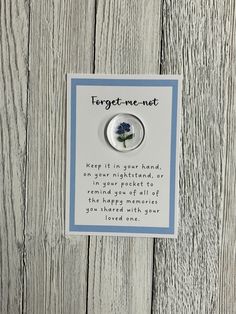 a brooch with a blue flower on it sitting on a wooden background that says forget me not