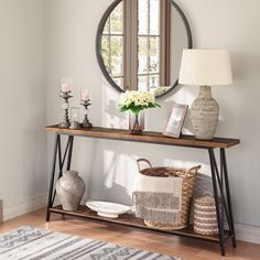 a table with a mirror, vase and basket on it in front of a window