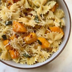 a bowl filled with pasta and vegetables on top of a white countertop next to a fork