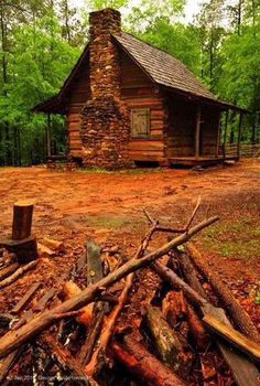 an old log cabin in the woods with logs piled on the ground next to it