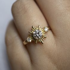 a woman's hand with a diamond ring on top of her finger and the sun in the middle