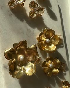 three gold flower brooches and two pearls on a white surface with a shadow