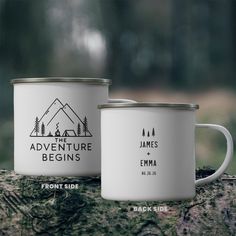 two white enamel mugs sitting on top of a tree trunk with the words adventure begins printed on them