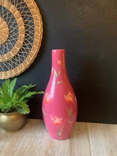 a pink vase sitting on top of a wooden table next to a potted plant