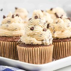 chocolate cupcakes with white frosting and chocolate chips on top, sitting on a plate