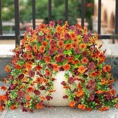 a potted plant with red and orange flowers on the ground next to a fence