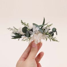 a hand holding a hair comb with white flowers and greenery on it's side