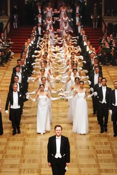 a man standing in front of a large group of people dressed in formal wear and tuxedos