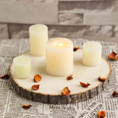 four lit candles sitting on top of a piece of wood next to leaves and newspaper