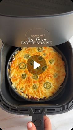 someone is holding up a pizza in an air fryer to show it's ingredients