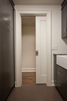 an empty hallway leading to a kitchen with stainless steel cabinets and white door knobs