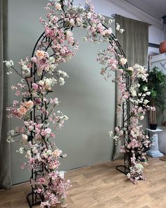 an arch decorated with pink and white flowers in front of a gray wall next to a wooden floor