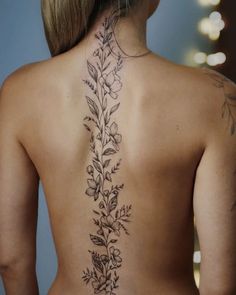 the back of a woman's neck with flowers and leaves tattooed on her lower back