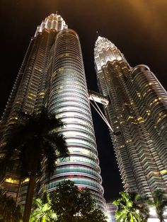 two very tall buildings lit up in the dark night sky with palm trees around them