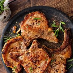 three pieces of meat sitting on top of a black plate next to garlic and herbs