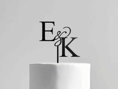 a white cake topped with a black monogrammed letter e and k on top of it