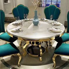 a round dining table with blue chairs and gold trim around the edges is surrounded by white marble flooring