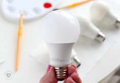 a person holding an energy saving light bulb in their hand next to a clock and other office supplies