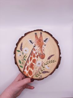 a hand holding a wooden slice with a giraffe painted on it