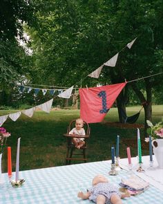 a baby sitting in a highchair at a picnic table with cake and candles