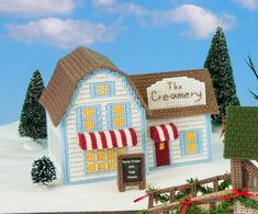 a crocheted christmas village with a store front and trees in the foreground