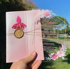 a person holding up a pink card with flowers on it and a gold medallion in the middle