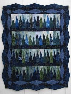 a quilted wall hanging on the side of a building with trees and mountains in it