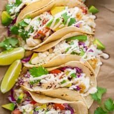 fish tacos with slaw, cilantro, and lime wedges on parchment paper