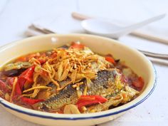 a bowl filled with fish and vegetables on top of a white table next to silverware