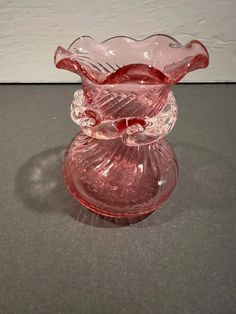 a pink glass vase sitting on top of a gray table next to a white wall