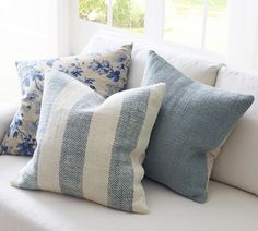 three blue and white pillows sitting on top of a couch next to a windowsill