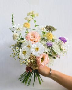 a person holding a bouquet of flowers in their hand with white and pink flowers on it