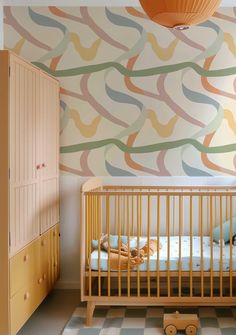 a baby's room with a crib, dresser and wallpaper in pastel colors