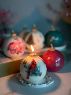 christmas ornaments are sitting on a table with a lit candle in the center and one is red, white and green