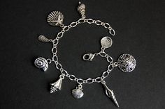 A collection of silver plated seashell themed charms have been dispersed around a shimmering silver plated bracelet chain in this handmade charm bracelet. This sea shell charm bracelet is then completed with a lobster clasp and a 1/2 inch of chain at the end for adjustable sizing. Charms in this bracelet include a starfish on a scallop shell charm, sand dollar charm, two scallop shell charms, conch shell charm, mussel shell charm, sea snail shell charm, long spiral shell charm, and spindle shell Sea Snail Shell, Handmade Charm Bracelets, Seashell Bracelet, Spiral Shell, Mussel Shell, Beach Bracelet, Sea Snail, Snail Shell, Beach Bracelets