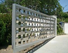 a large metal fence sitting on the side of a road next to a tree and bushes