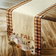 a fall table runner with pumpkins and leaves is hanging from a wooden table top