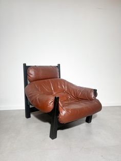 a brown leather chair sitting on top of a white floor next to a black wooden frame