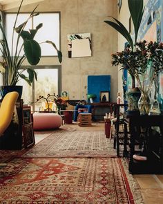 a living room filled with lots of furniture and plants on top of rugs in front of windows