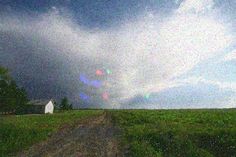 a dirt road in the middle of a green field under a cloudy sky with sunbeams