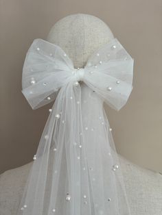 the back of a white veil with pearls on it and a bow at the top