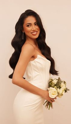 a woman in a white dress holding a bouquet of flowers and smiling at the camera