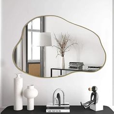 a mirror sitting on top of a table next to a lamp and vase with flowers