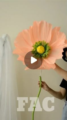 a woman holding a large pink flower in front of a white wall with the word fac on it