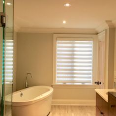 a large white bath tub sitting next to a window in a bathroom with wooden floors